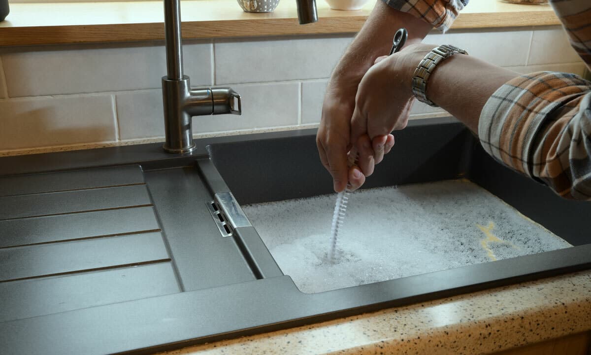 Someone using a plumber snake on a backed up kitchen sink