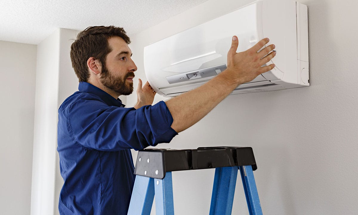 An HVAC technician on a ladder placing the head cover on a ductless mini split