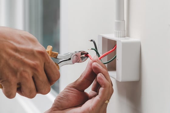 An up close photo of a person cutting wires in an outlet box in a home