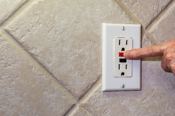 A photo of a person resetting the GFCI outlet on a wall