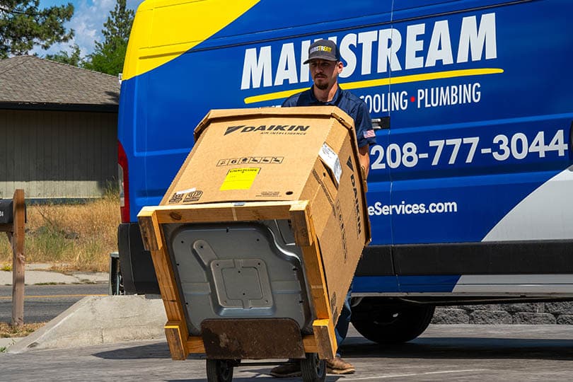 A Mainstream HVAC technician bringing an AC unit into a home