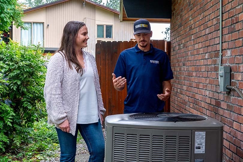 A Mainstream technician talking over options with a customer in front of an air conditioner.