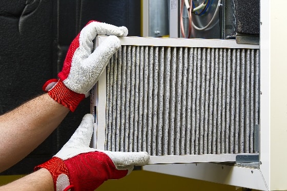 An up close image of a dirty air filter being pulled out of an HVAC unit