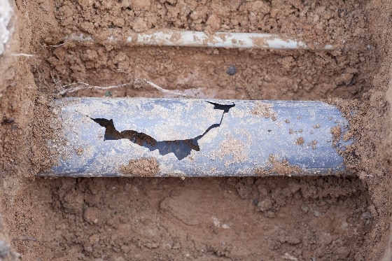 An up close photo of a cracked pipe in the ground