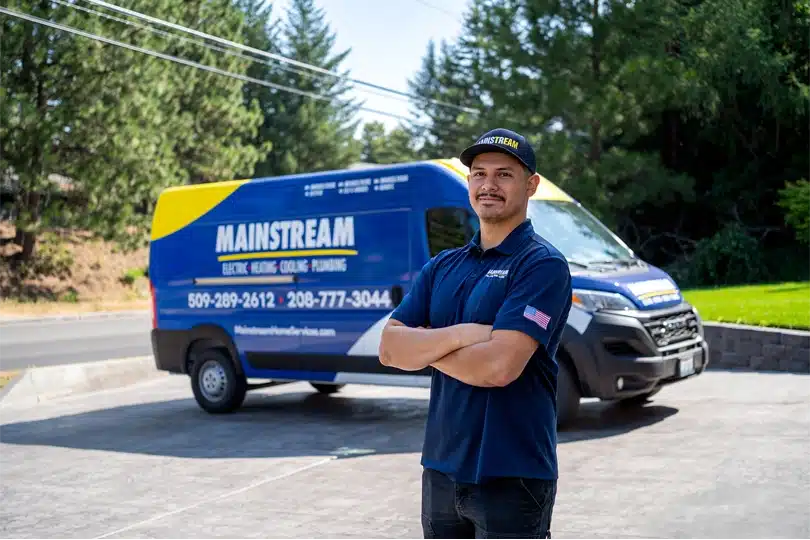 A Mainstream Electric, Heating, Cooling, & Plumbing technician posing with confidence in front of work van