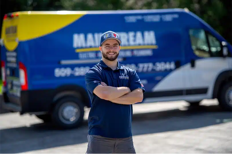 A Mainstream Electric, Heating, Cooling, & Plumbing technician posing in front of work van