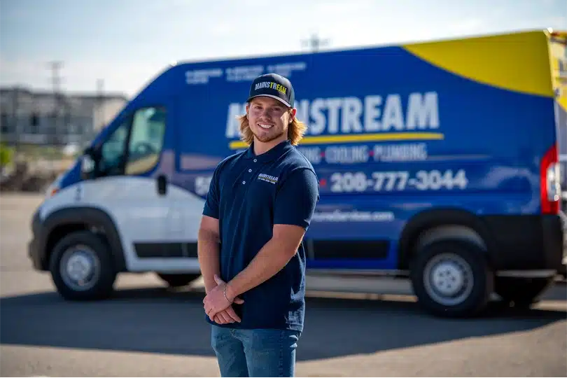 A technician from Mainstream Electric, Heating, Cooling, & Plumbing stands in front of a work van