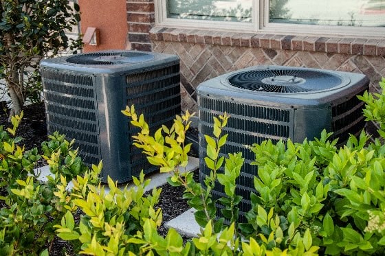 Two Outdoor HVAC Units Near Bushes