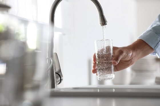 A person filling up a glass of clean water at a kitchen faucet