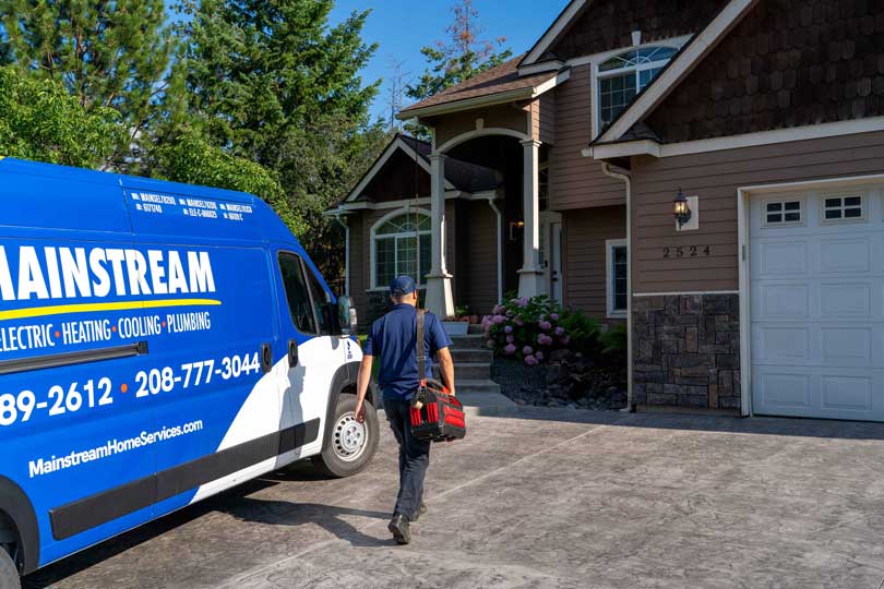 A Mainstream van parked in a home's driveway with the technician walking toward the door