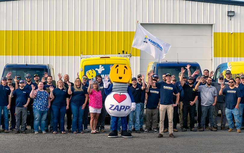 The team of Mainstream in front of their building waving at the camera
