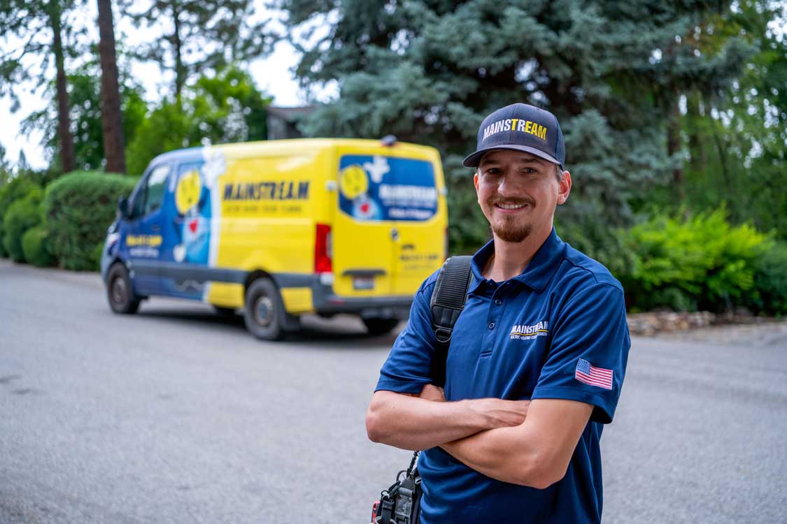 An HVAC technician from Mainstream standing in front of the Mainstream company van.