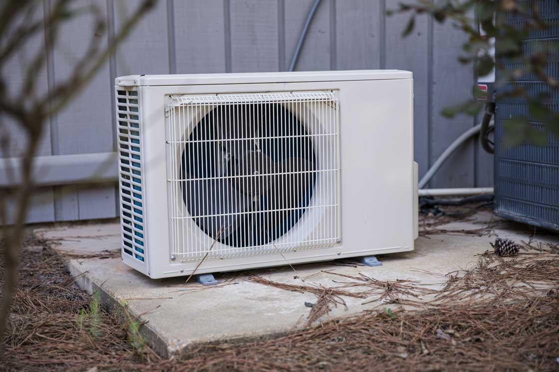 Mini split heat pump on a slab outside with pine needles around it