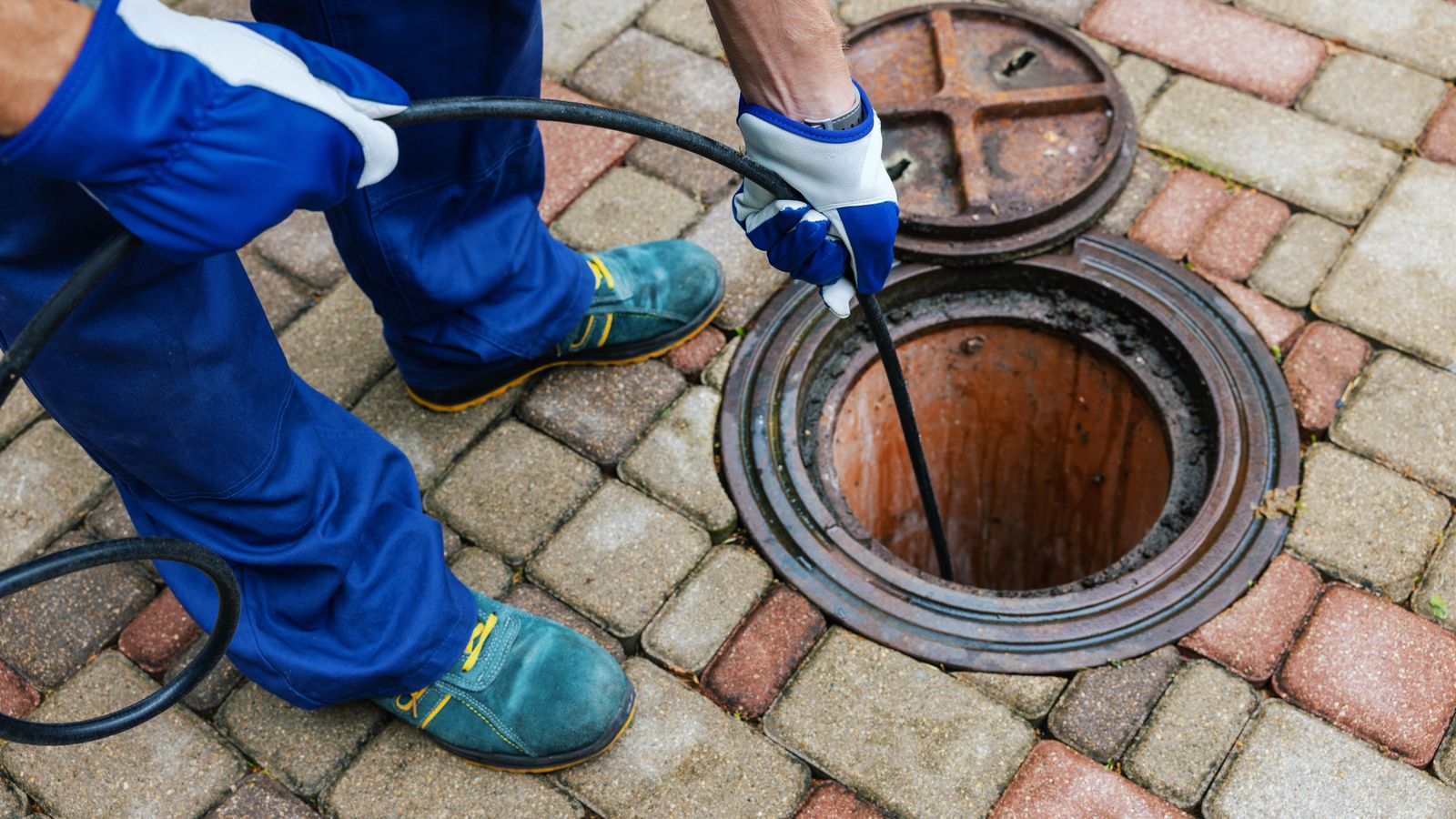 A plumber working to clear a drain outside a home