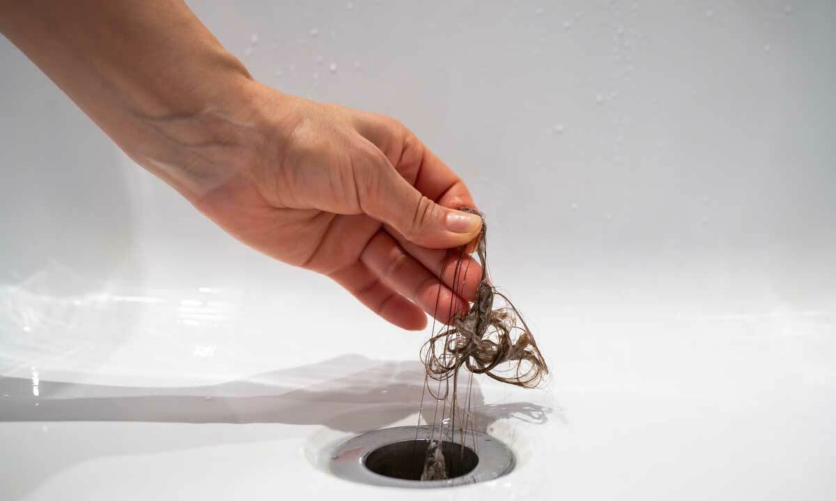 A person removing hair from a clogged tub drain