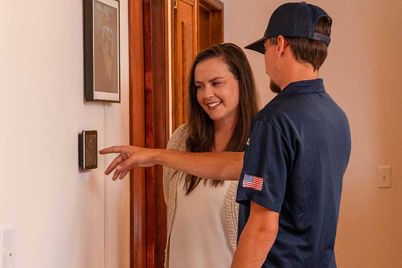 A Mainstream HVAC technician showing a customer how to use their newly installed smart thermostat