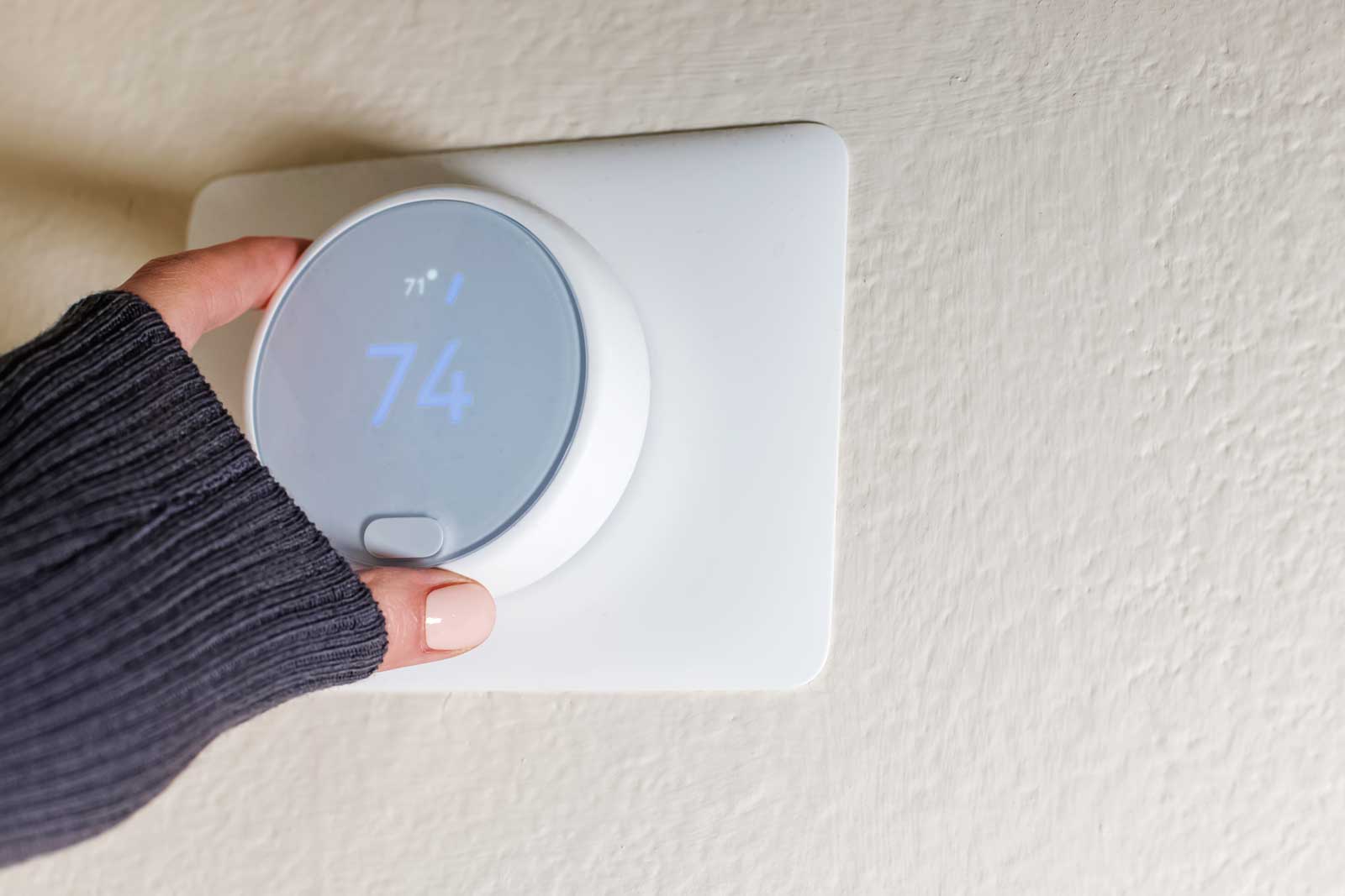 A sleeved hand turning up the temperature on a smart thermostat