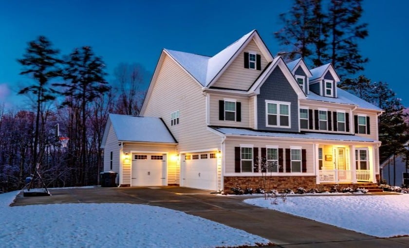 A single family home as viewed from the street in winter at night with the front lights on